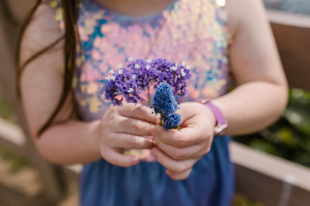 girl in blue and pink floral tank top holding purple flower
