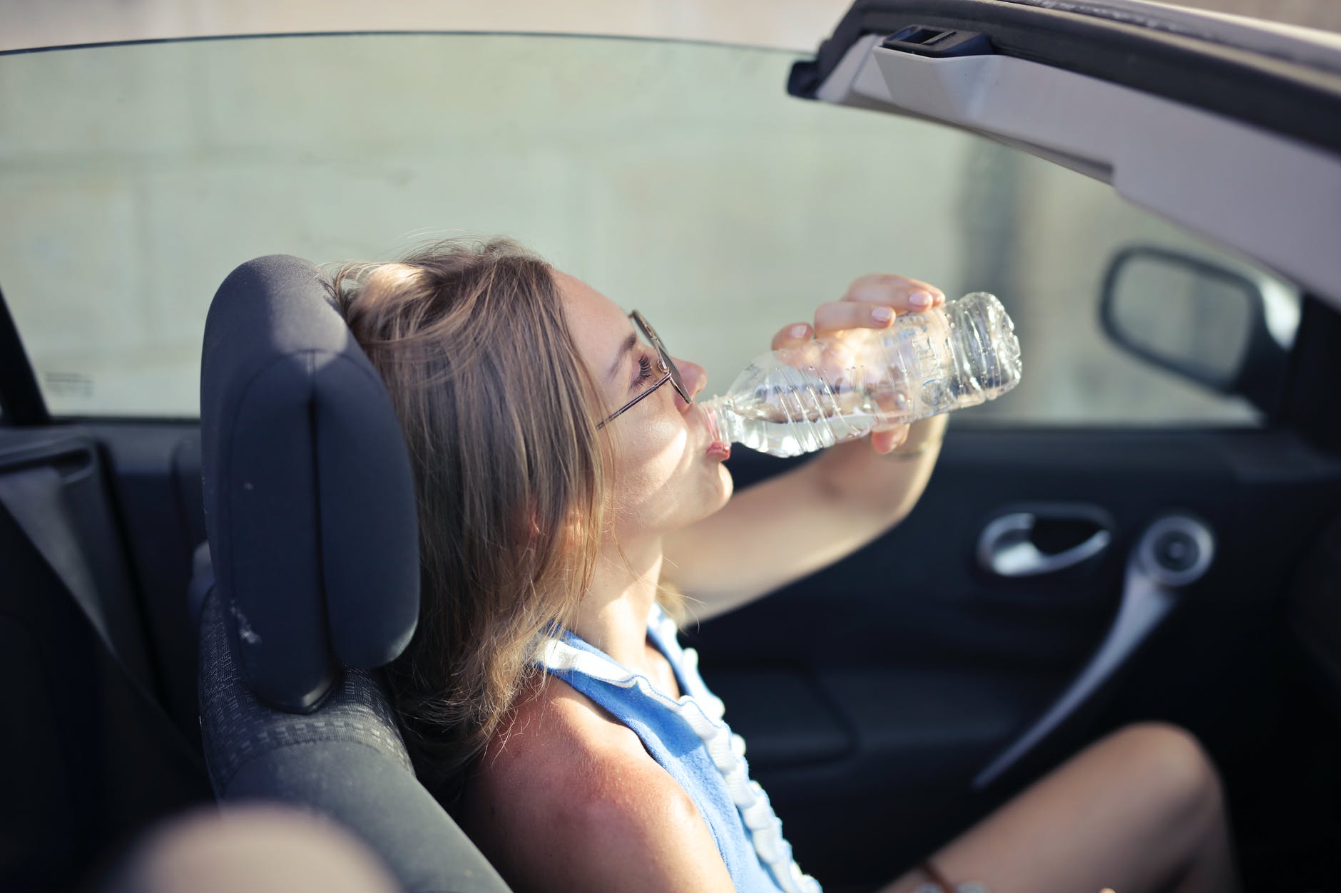 adult female drinking water in convertible car in city